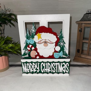 May include: A wooden Christmas decoration featuring Santa Claus with a red hat and white beard, holding a candy cane. The decoration includes green trees, blue birds, and the words "MERRY CHRISTMAS" in white on a green background.