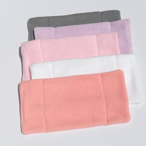 May include: A stack of five fleece headbands in various colors: gray, lavender, pink, white, and peach. Each headband is rectangular with a seam down the middle and a soft, fuzzy texture. The headbands are arranged in a slightly overlapping manner.
