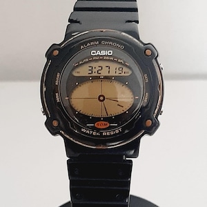 May include: Black Casio digital watch with a round face. The watch displays the time 3:27:19. The watch has the words "ALARM CHRONO", "CASIO", and "WATER RESIST" printed on the face. The watch band is black.
