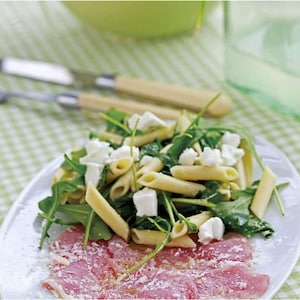 Puede incluir: Un plato blanco contiene una ensalada fresca con pasta penne, rúcula y queso blanco. Debajo, carne finamente cortada espolvoreada con queso rallado. El fondo incluye un mantel a cuadros verdes y blancos y cubiertos.