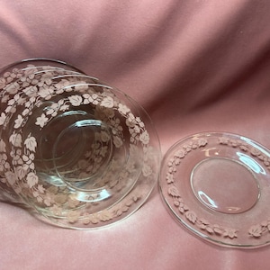 May include: A set of four clear glass dessert plates with a delicate floral design. The plates have a scalloped edge and are perfect for serving desserts or appetizers.