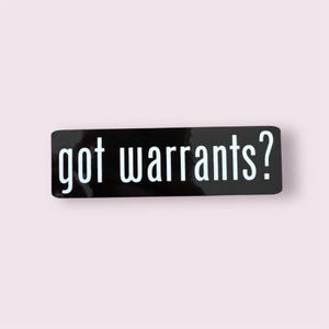 May include: A rectangular black sticker with the words "got warrants?" in white, sans-serif font. The sticker has a glossy finish and is set against a light pink background.