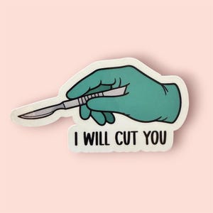 May include: A sticker featuring a teal-colored gloved hand holding a silver scalpel. The text "I WILL CUT YOU" is printed in black capital letters below the hand and scalpel illustration. The background is a light pink color.