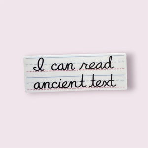May include: A rectangular sticker featuring a white background with blue and red horizontal lines resembling handwriting practice paper. The black cursive text reads I can read ancient text, positioned across two lines on the lined surface.