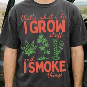 May include: Dark gray t-shirt with the text "that's what I do, I GROW stuff and I SMOKE things" in red and green. The shirt features cannabis leaf and plant graphics, along with a smoking pipe illustration.