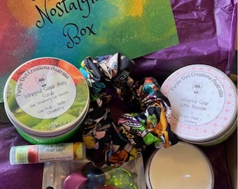 May include: A 90s nostalgia themed gift box with a purple background. The box contains a green jar of whipped sugar body scrub, a small jar of whipped soap, a lip balm, a candle, a scrunchie, and a bag of bath bombs. The jar of whipped sugar body scrub has the text "Whipped Sugar Body Scrub" and "Kiwi Strawberry Lip Smacker" on the label. The jar of whipped soap has the text "Whipped Soap Little Blossom" on the label. The lip balm has the text "Froot Loops" on the label. The candle is white and round. The scrunchie is black and has a colourful cartoon pattern. The bath bombs are colourful and round.