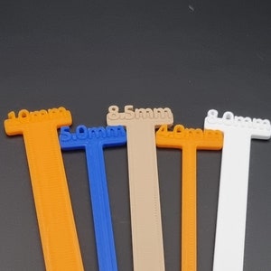May include: Five different coloured plastic measuring sticks with the measurements 10mm, 5.0mm, 8.5mm, 4.0mm, and 8.0mm printed on them.