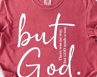 May include: Crimson-colored t-shirt with the words "but God" in white script. The text "There was no way, but GOD made a way" is also printed on the shirt. The shirt is paired with denim shorts, shoes, and a hat.