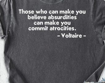May include: A charcoal gray t-shirt with the quote "Those who can make you believe absurdities can make you commit atrocities. - Voltaire -" printed in white. The shirt is paired with denim shorts, shoes, and a hat.
