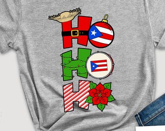 May include: A heather gray t-shirt with a festive "HO HO HO" design. The design incorporates Christmas elements and the Puerto Rican flag. The shirt is surrounded by holiday decorations, including a wreath, a bow tie, and a gift box.