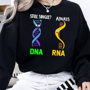 May include: Black sweatshirt with the text "STILL SINGLE? ALWAYS" above cartoon DNA and RNA strands. The DNA strand is blue and purple, and the RNA strand is yellow. The word "DNA" is green, and "RNA" is orange.