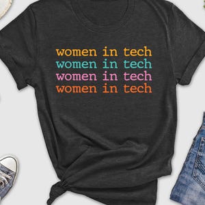 May include: A dark grey t-shirt with the text "women in tech" repeated four times in different colors: orange, teal, pink, and orange.