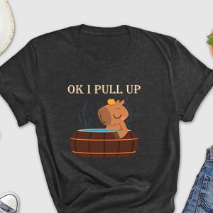 May include: A dark gray t-shirt with a cartoon capybara in a hot tub. The text "OK I PULL UP" is printed on the shirt.