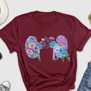 May include: A maroon t-shirt with a floral design of two kidneys. The flowers are in shades of pink, purple, and blue.