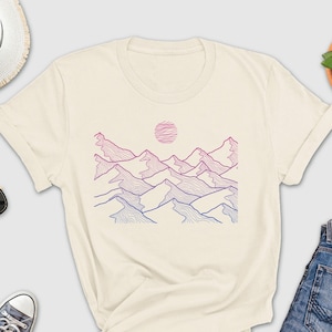 May include: A cream colored t-shirt with a graphic of a mountain range with a pink and blue gradient and a sun in the background.