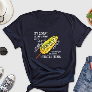 May include: A navy blue t-shirt with a white graphic of a corn on the cob with the text "It's corn! A big lump with knobs, it has the juice, I can't drive after eating it, I mean look at this thing!"