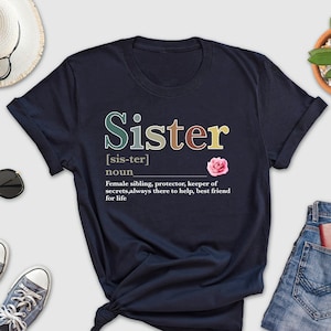 May include: Navy blue t-shirt with the word "Sister" in colorful letters and a definition below. The definition reads: "[sis-ter] noun Female sibling, protector, keeper of secrets, always there to help, best friend for life"