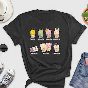 May include: A dark gray t-shirt with a graphic of cartoon animals holding bubble tea cups. The text on the shirt reads "PAR-TEA", "GUILT-TEA", "ROBAL-TEA", "CELEBRA-TEA", "ANXIE-TEA", "BEST-TEA", and "SMART-TEA".