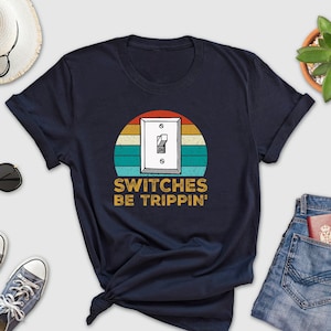May include: A navy blue t-shirt with a vintage-style graphic of a light switch with the text "SWITCHES BE TRIPPIN'" underneath.