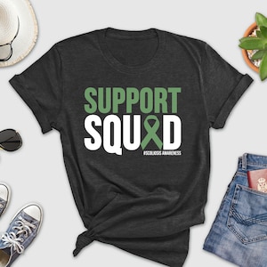 May include: A dark grey t-shirt with white text that reads "SUPPORT SQUAD" with a green ribbon and the hashtag "#SCOLIOSIS AWARENESS".