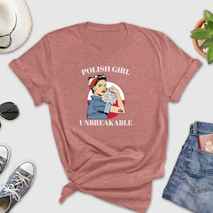 May include: A heathered red t-shirt with the text "POLISH GIRL UNBREAKABLE" and a graphic of a woman flexing her arm. The shirt is styled with blue jeans, sunglasses, a straw hat, and sneakers.