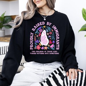 A woman wearing a black sweatshirt with a colorful graphic design and text printed on it.