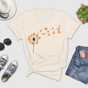a white t - shirt with a dandelion on it next to a pair