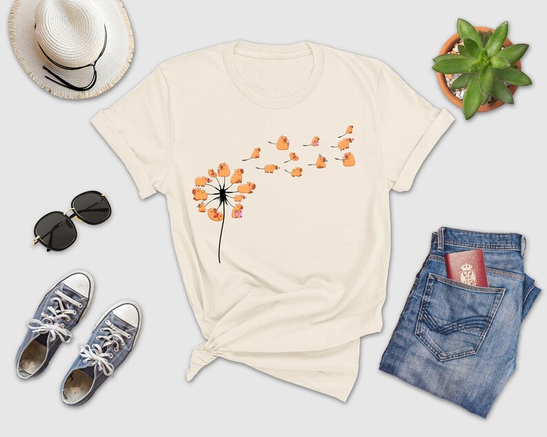 a white t - shirt with a dandelion on it next to a pair