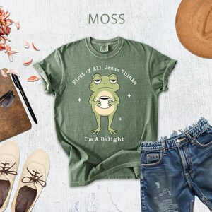 a green t-shirt with a cartoon frog holding a cup, a pair of blue jeans, a brown hat, sunglasses, a notebook, and a pair of white shoes.