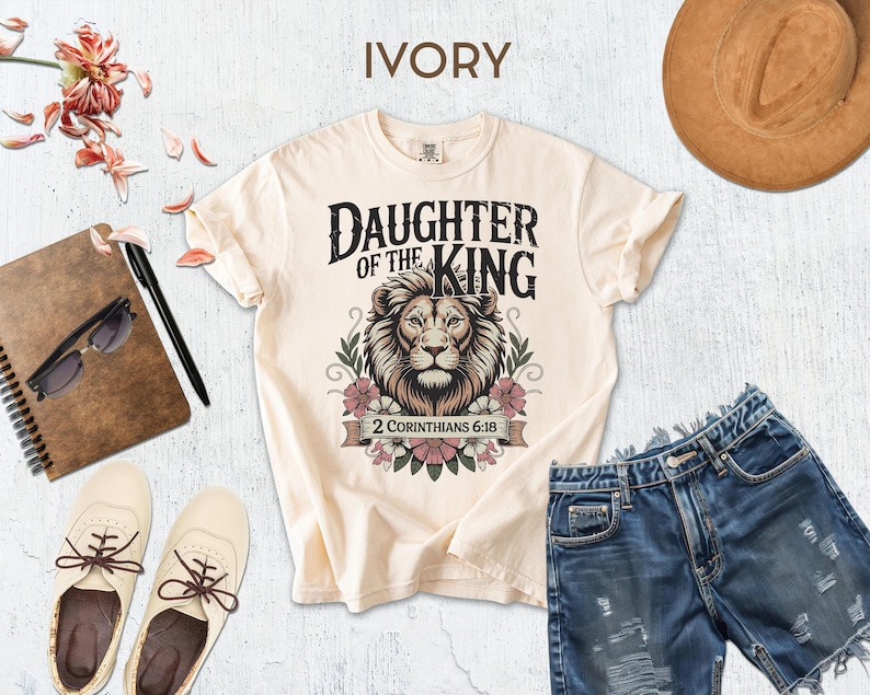 a casual outfit consisting of a white t-shirt with a lion graphic, denim shorts, and a brown hat, along with some accessories such as sunglasses, a notebook, and a pair of shoes.