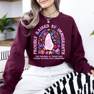 A woman wearing a burgundy sweatshirt with a graphic design on it, sitting on a couch with a zebra print pillow.
