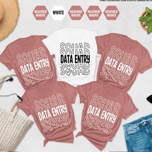 May include: A flat lay featuring a collection of t-shirts. The shirts are in heather mauve and white, with the words "SQUAD DATA ENTRY" printed on them. Accessories include sunglasses, a straw hat, and a woven tote bag.