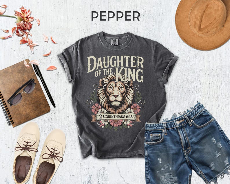 a casual outfit consisting of a gray t-shirt with a lion graphic, distressed denim shorts, a brown hat, sunglasses, a notebook, and a pair of white sneakers.