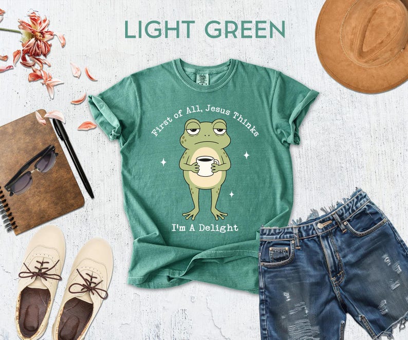 a green t-shirt with a cartoon frog, a pair of denim shorts, a hat, sunglasses, a notebook, and a cup, all arranged on a white background.