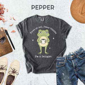 a gray t-shirt with a frog graphic, a pair of denim shorts, a hat, sunglasses, a notebook, and a pair of white sneakers.