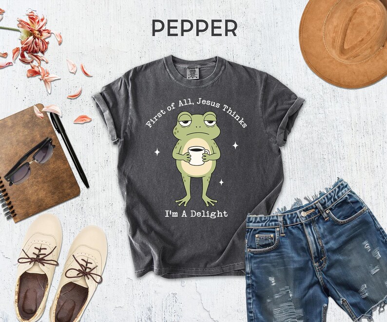 a gray t-shirt with a frog graphic, a pair of denim shorts, a hat, sunglasses, a notebook, and a pair of white sneakers.