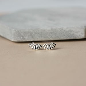 May include: A pair of silver fan-shaped earrings. The earrings are small and delicate, and they have a simple, elegant design.