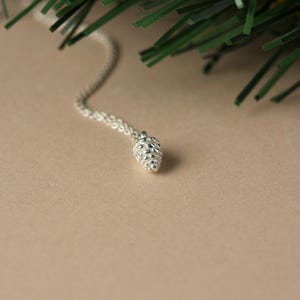 May include: A silver necklace with a small, detailed pine cone pendant.