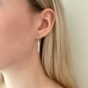 May include: Silver hammered bar earrings hanging from a person's ear.