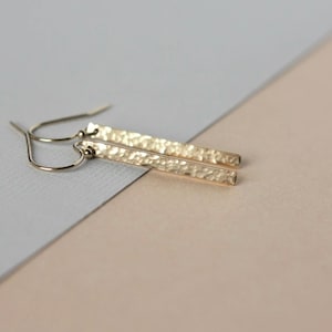 May include: A pair of gold hammered bar earrings with a simple hook fastening.