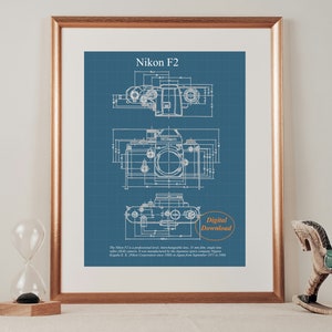 Puede incluir: Una impresión de descarga digital de una ilustración de estilo plano de una cámara Nikon F2. La impresión está sobre un fondo azul con líneas y texto blancos. El texto dice "Nikon F2" y "Descarga digital".