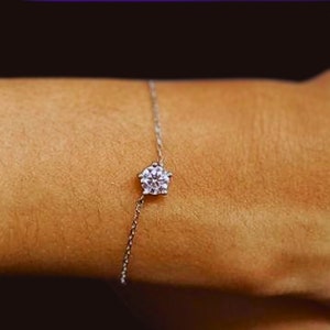 May include: A delicate silver chain bracelet with a single, round, clear gemstone in the center.