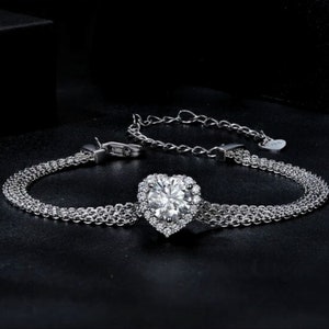 May include: A silver bracelet with a heart-shaped pendant featuring a large, clear cubic zirconia surrounded by smaller cubic zirconia stones.