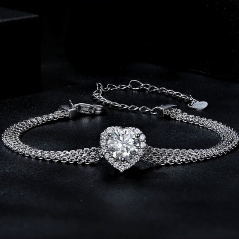 May include: A silver bracelet with a heart-shaped pendant featuring a large, clear cubic zirconia surrounded by smaller cubic zirconia stones.