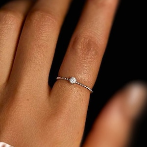 May include: A delicate silver ring with a single, small, round diamond set in the center.