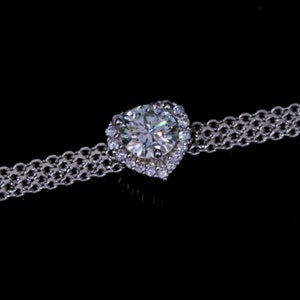 May include: A silver chain bracelet with a large, clear heart-shaped diamond surrounded by smaller diamonds.