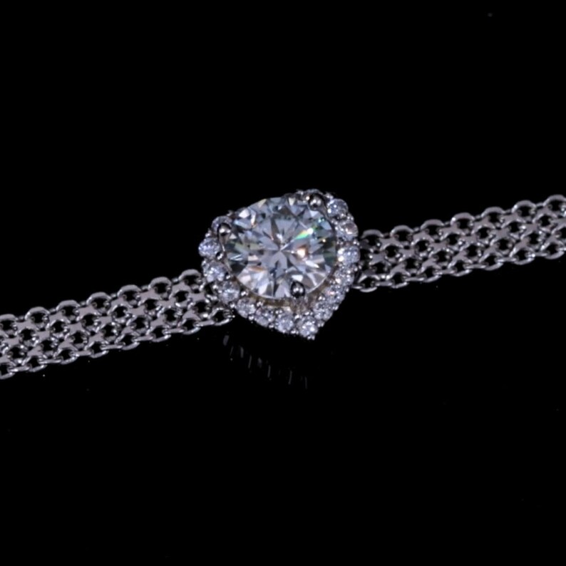 May include: A silver chain bracelet with a large, clear heart-shaped diamond surrounded by smaller diamonds.