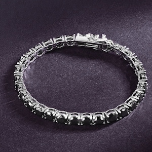 May include: A silver tennis bracelet with black round stones.