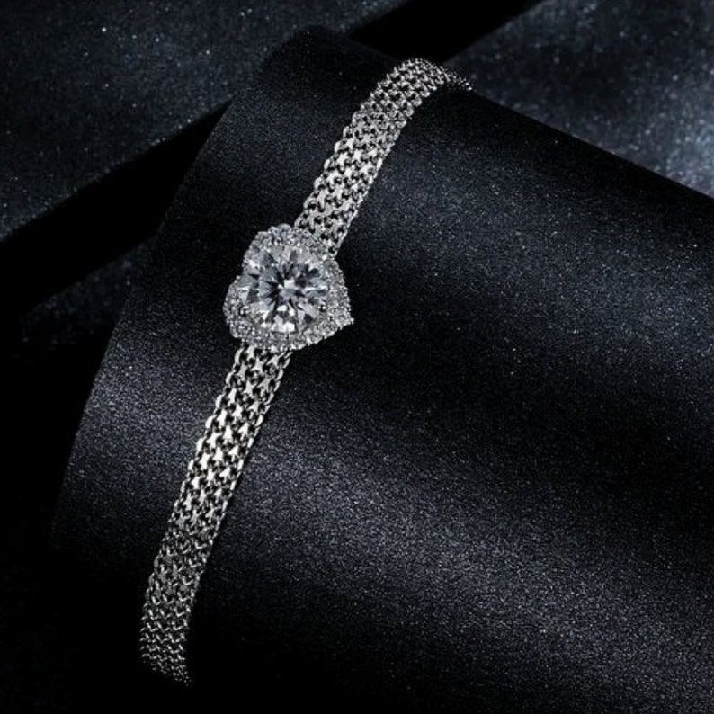May include: A silver bracelet with a heart-shaped diamond pendant. The bracelet is made of a delicate chain and the diamond is surrounded by smaller diamonds.