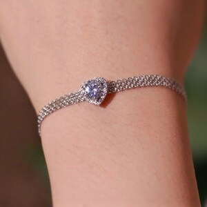 May include: A silver chain bracelet with a heart-shaped pendant featuring a large, clear cubic zirconia stone.